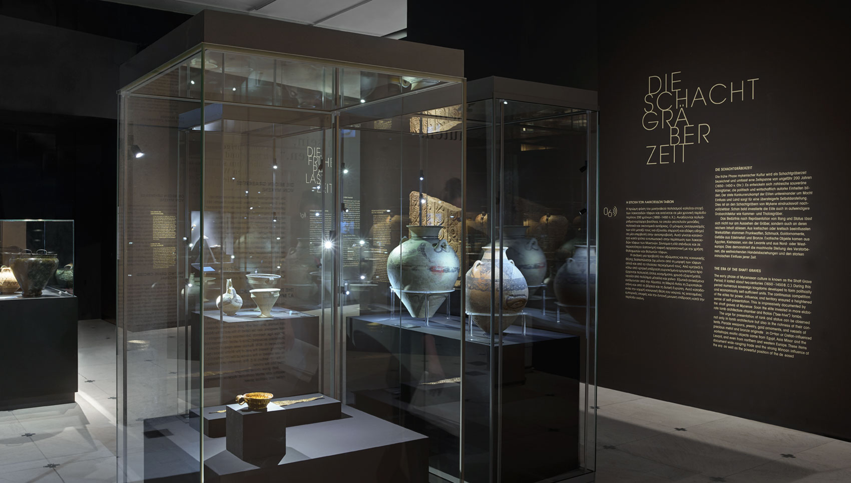 Dunkler Ausstellungsraum mit Wandgrafiken und verschiedenen Exponaten