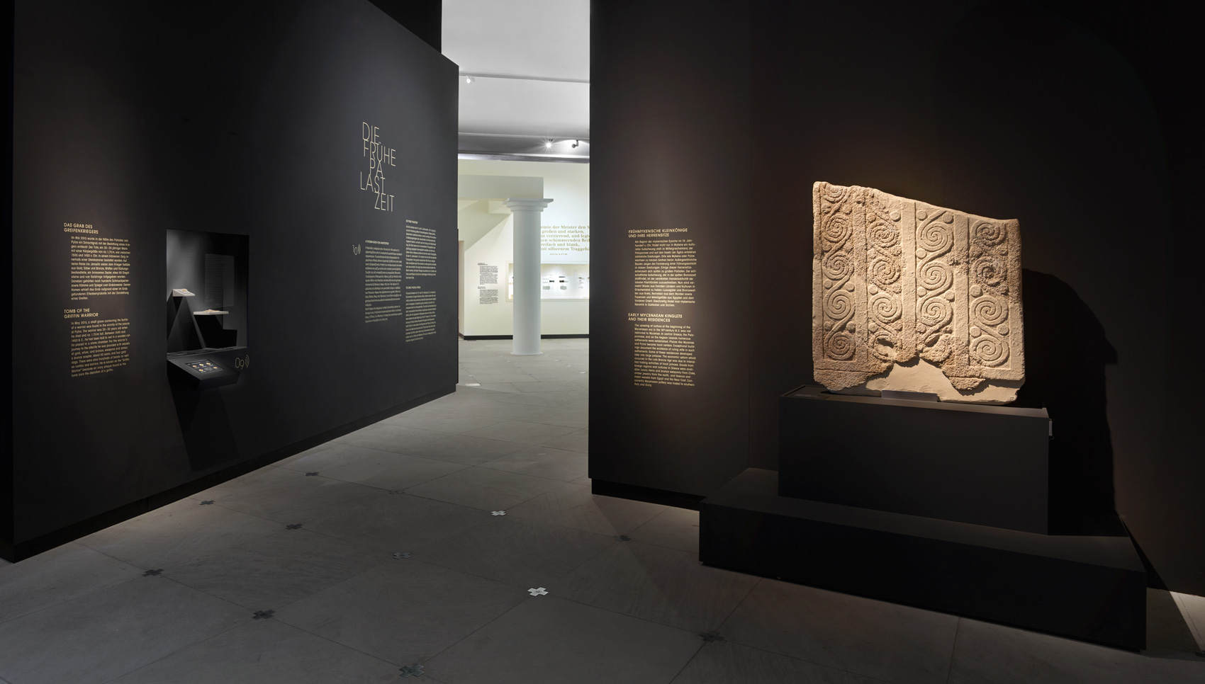 Dunkler Ausstellungsraum mit Wandgrafiken und verschiedenen Exponaten