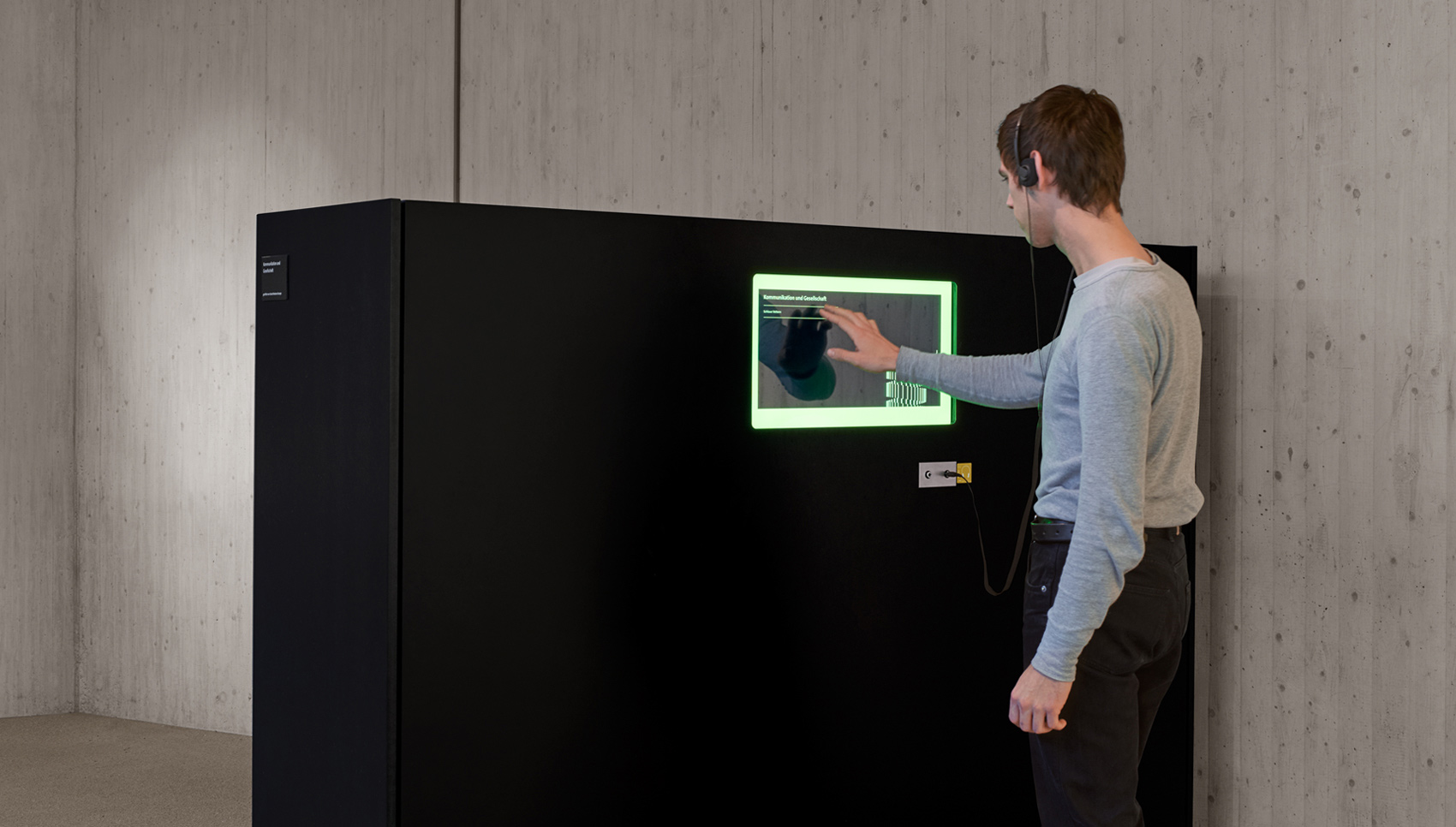 Mann steht vor interaktivem Ausstellungsobjekt mit Touch-Display und Kopfhörern