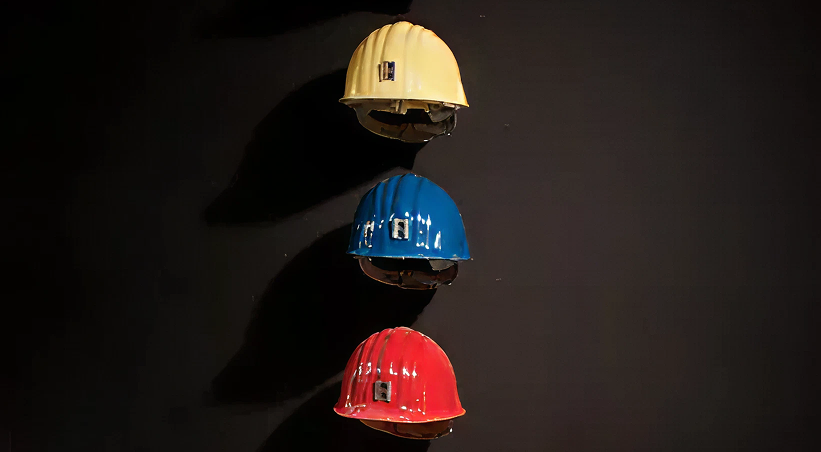 Ausstellungsinstallation, bei der bunte Sicherheutshelme übereinander vor einer schwarzen Wand angeordnet sind