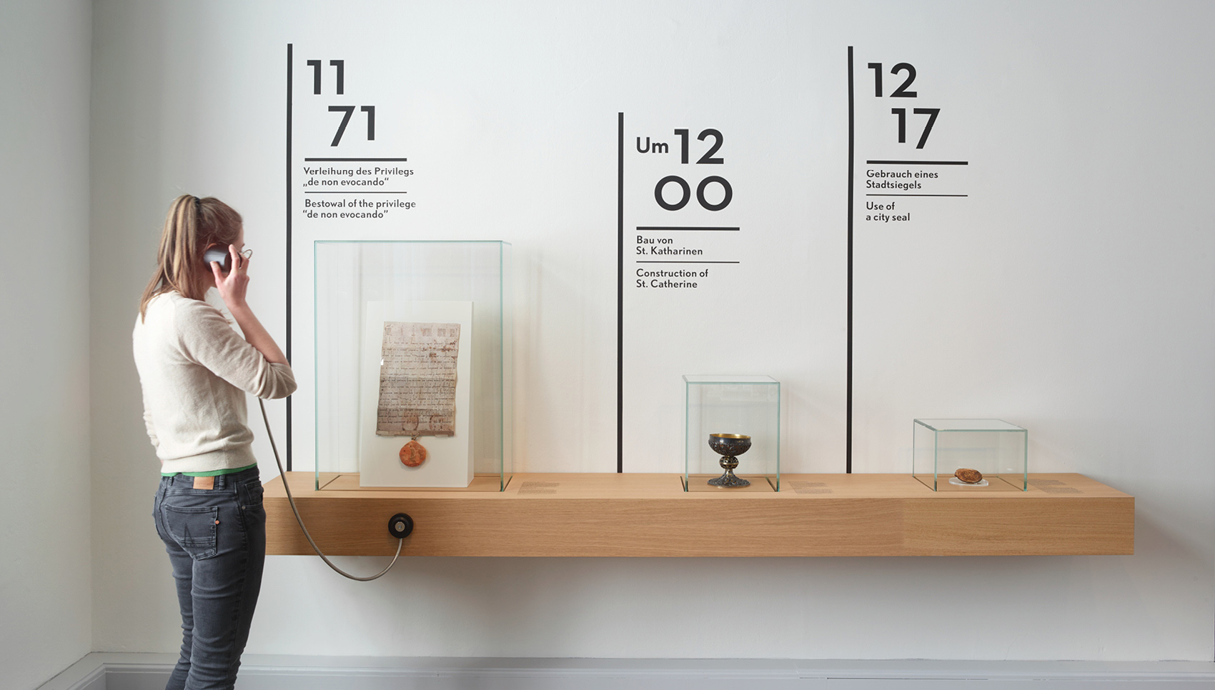 Person steht vor ausgestellten Exponaten, die auf einem hölzernem Regal stehen.