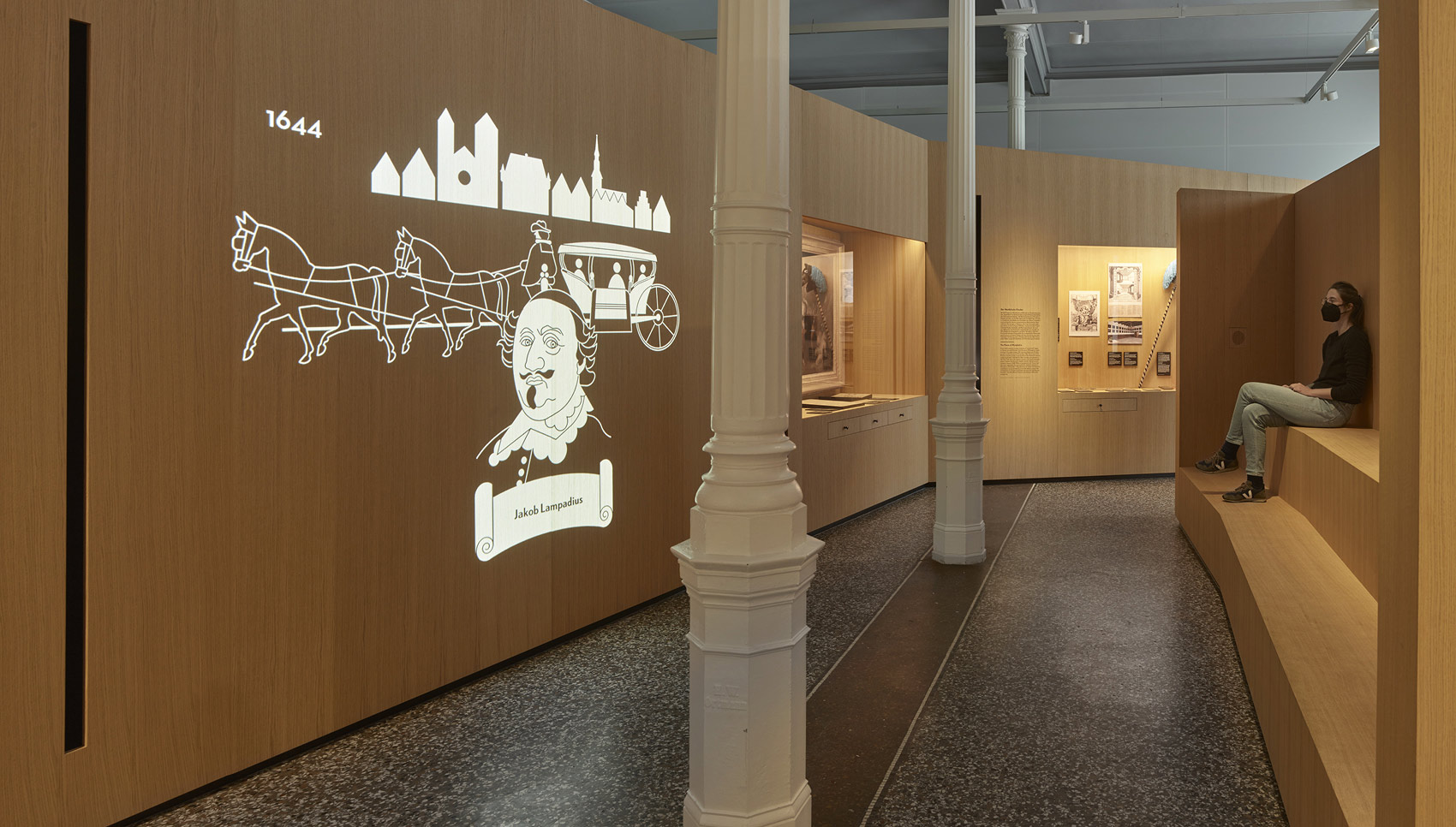 Person sitzt auf Sitgelegenheit aus Holz und schaut sich eine Projektion auf eine gegenüberliegenden hölzernen Wand an