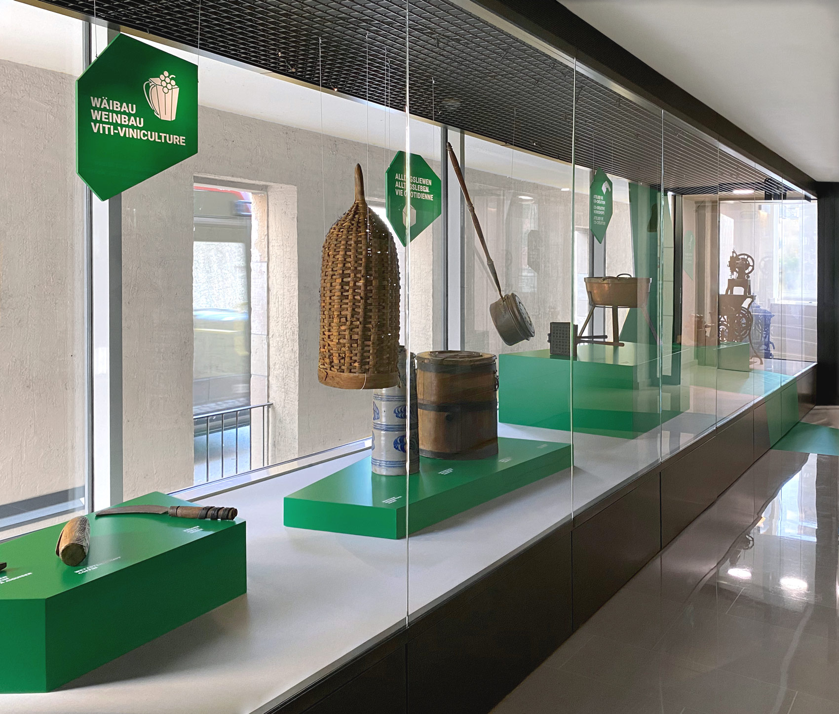 Verschiedene Exponate auf grünen Podesten mit grünen Hängeschildern