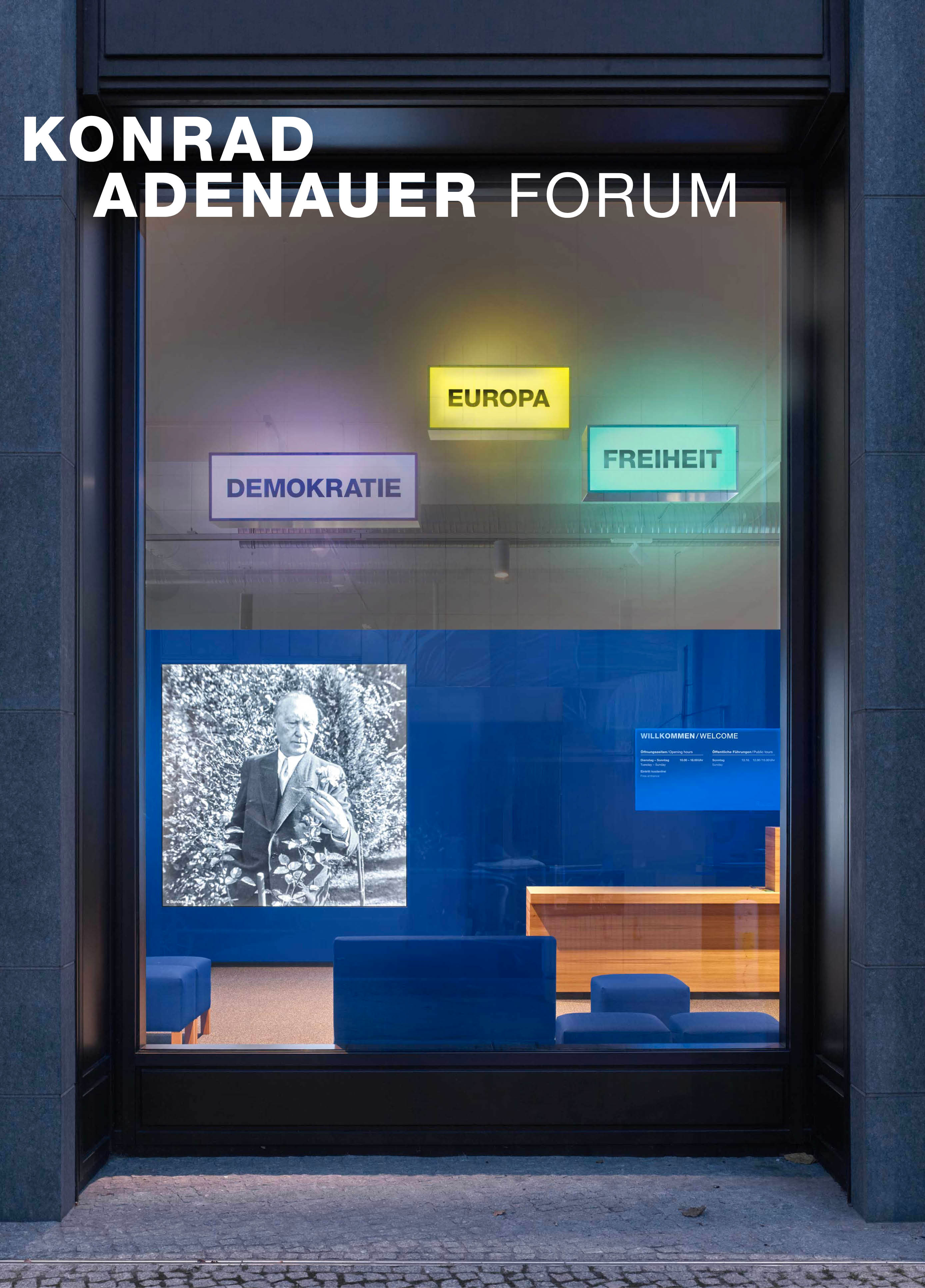 Schaufenster von außen mit 3 Leuchtboxen "Demokratie", "Europa" und "Freiheit". Dahinter eine blaue Wand mit einem großen Display auf dem Konrad-Adenauer in schwarz-weiß zu sehen ist.