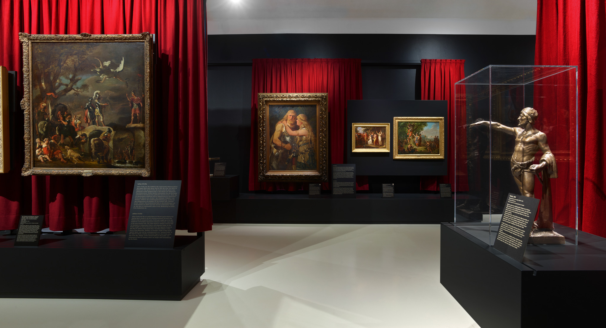 Ausstellungsraum mit verschiedenen Exponaten und roten Vorhängen, die von der Decke hängen