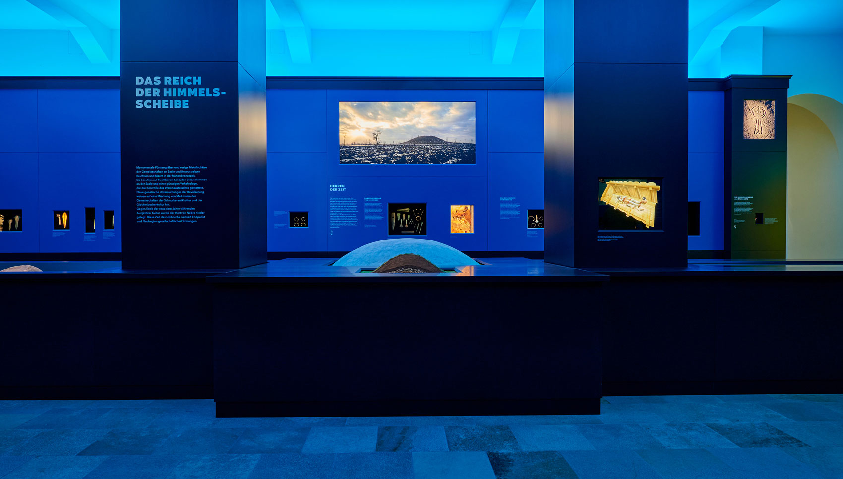 Ausstellungsraum mit Ausstellungsmöbeln und Exponaten in blauem Licht