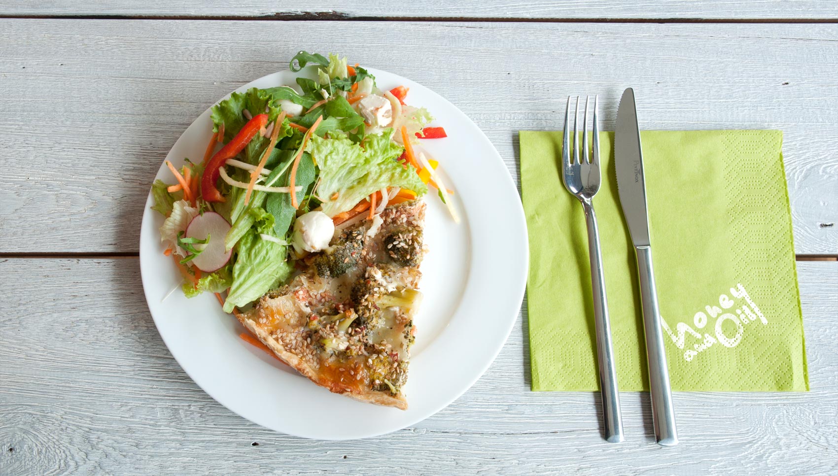 Quiche auf einem Teller. Daneben Gabel und Messer auf einer Serviette mit Logo