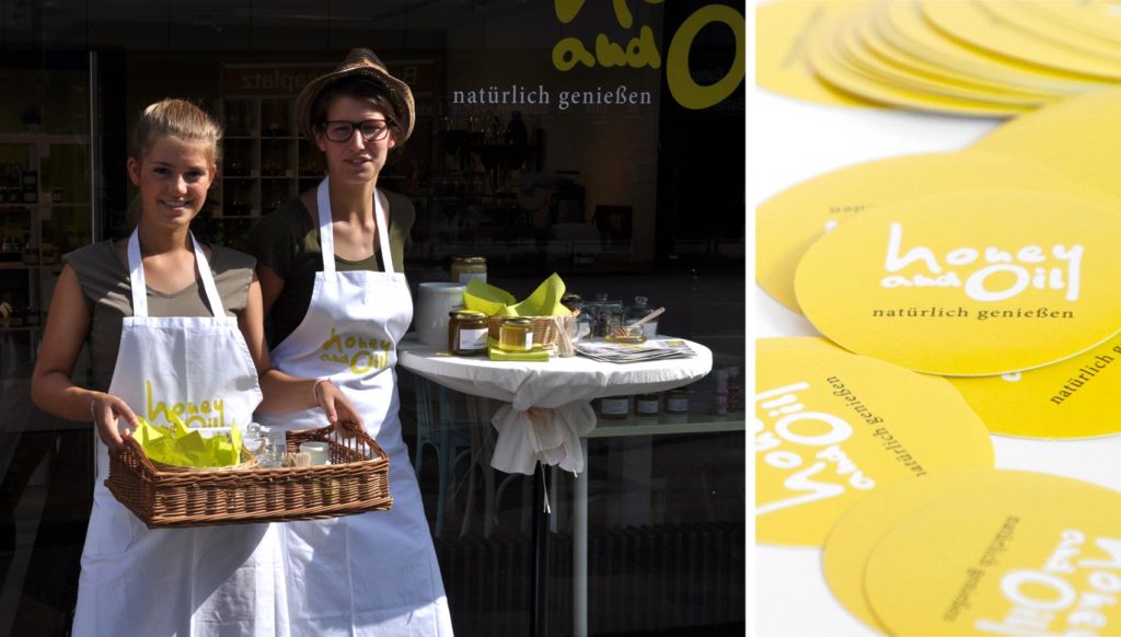 Zwei Personen stehen vor dem Ladenlokal und tragen jeweils eine weiße Schürze mit dem Logo. Zweites Bild zweigt Aufkleber mit Logo
