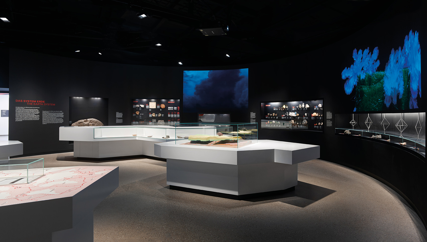 Dunkler Ausstellungsraum mit weißen Ausstellungsmöbeln und verschiedenen Exponaten.