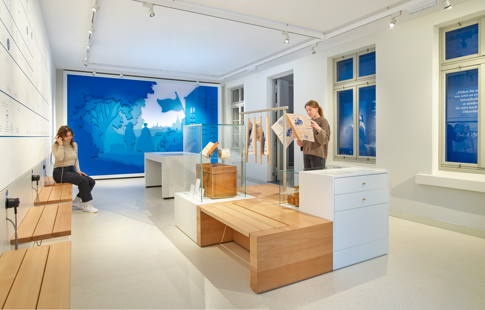 Ausstellungsraum mit zwei Personen, Ausstellungsmöbeln und verschiedenen Exponaten