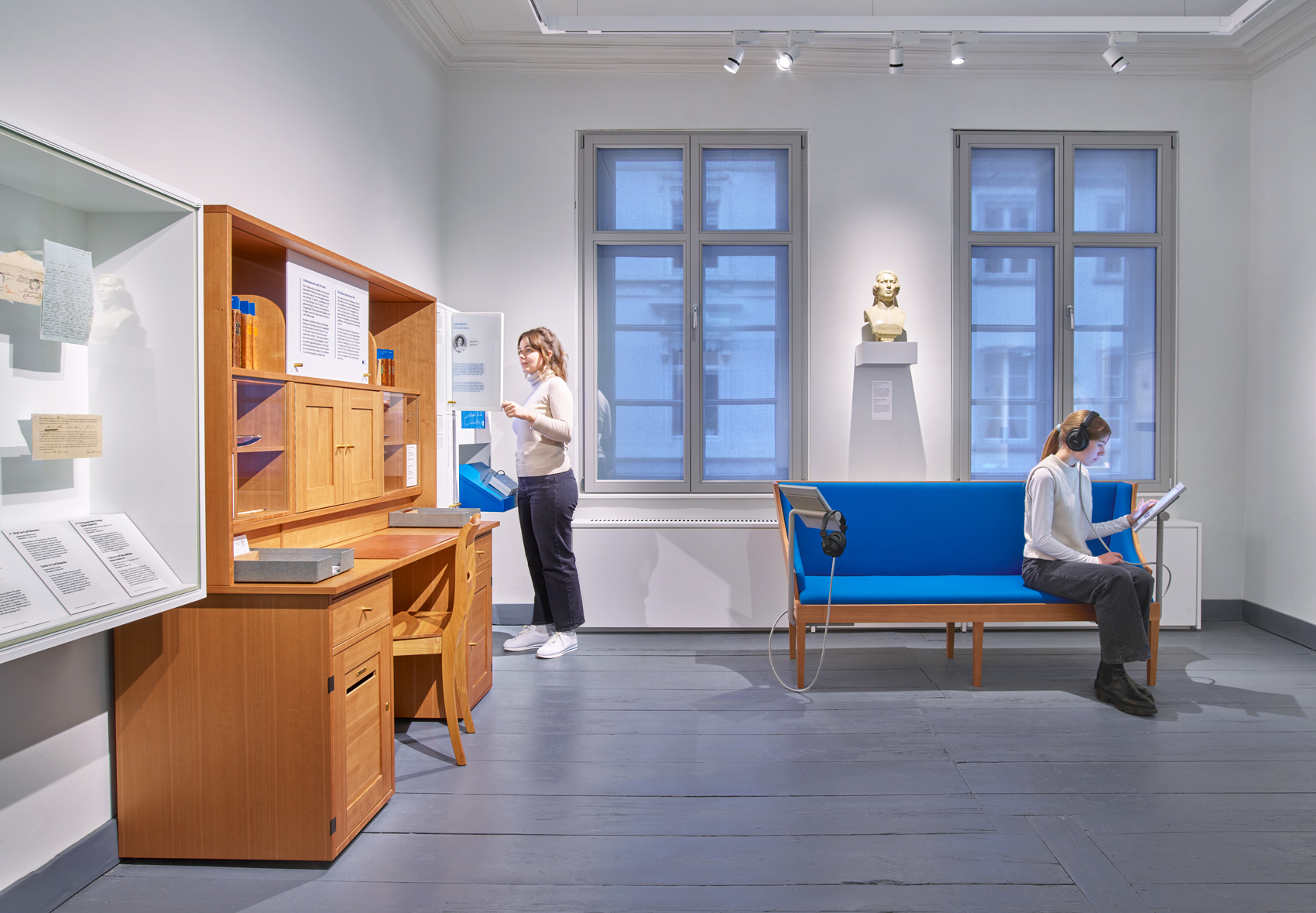 Zwei Personen im Ausstellungsraum mit Ausstellungsmöbeln und verschiedenen Exponaten