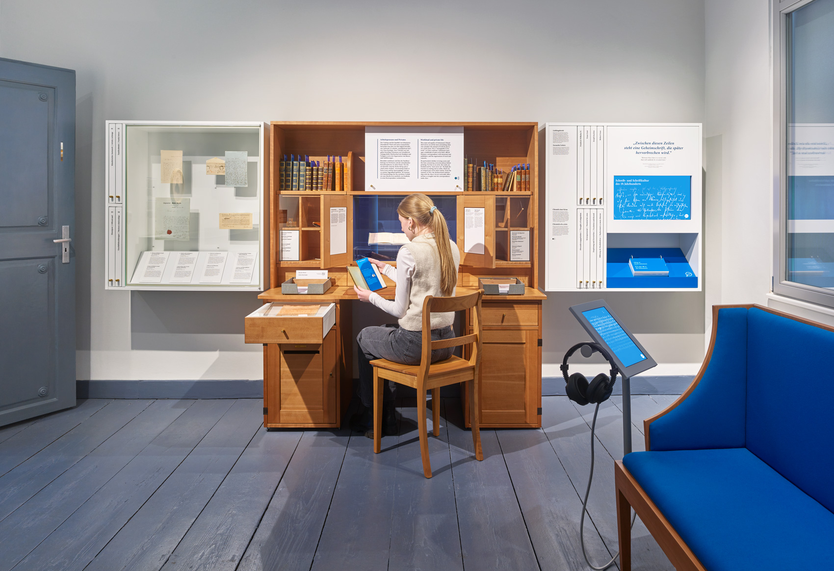 Person im Ausstellungsraum mit Ausstellungsmöbeln und verschiedenen Exponaten