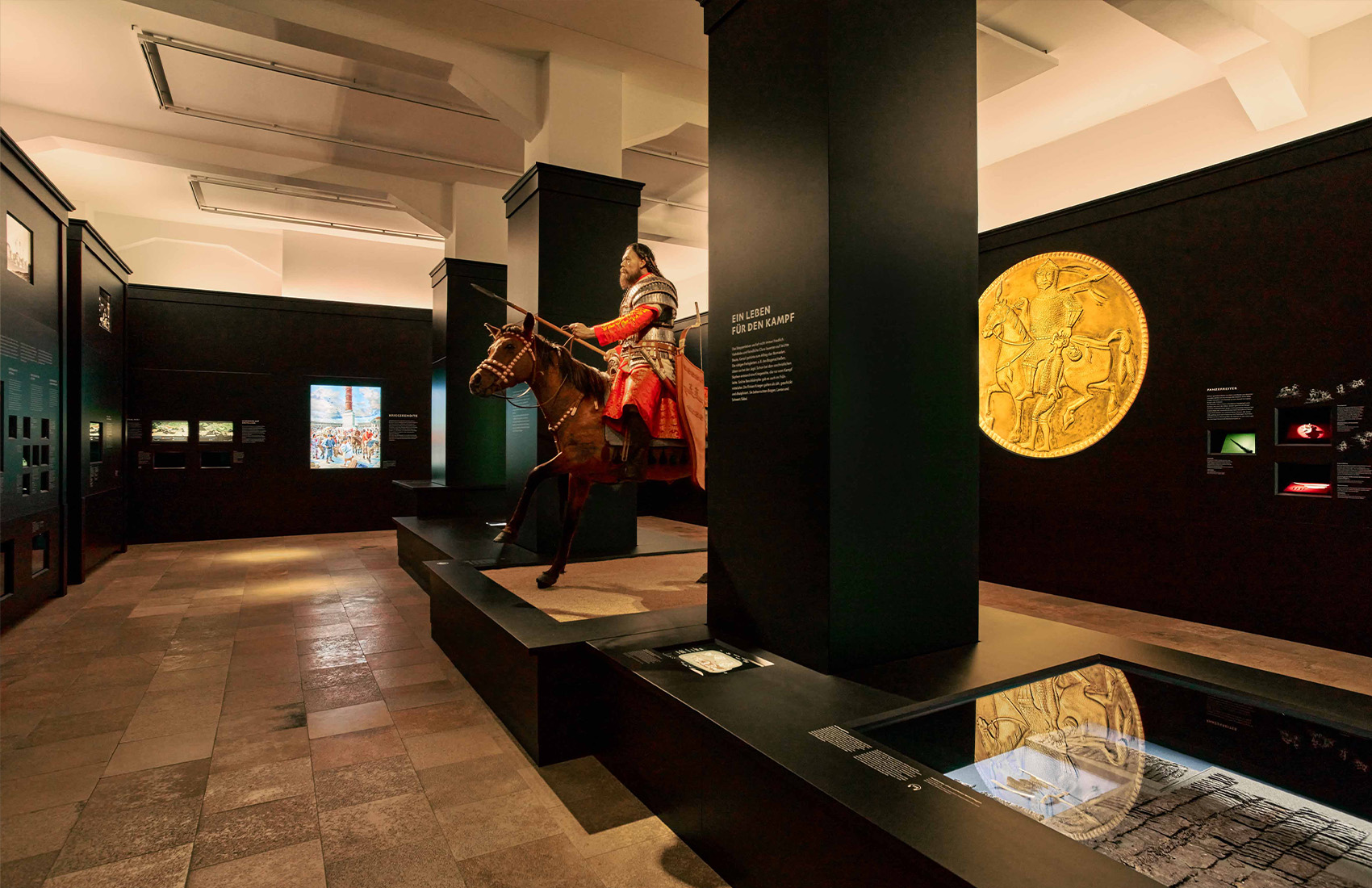 Ausstellungsraum mit schwarzen Ausstellungsmöbeln, verschiedenen Exponaten und einer großen nachgebildeten Reiterfigur, die zentral im Raum angeordnet ist.