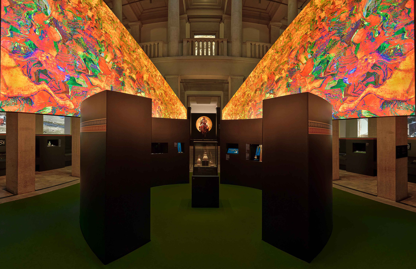 Ausstellungsraum mit schwarzen Ausstellungsmöbeln, verschiedenen Exponaten und einer großen hinterleuchteten Grafik im Luftraum.