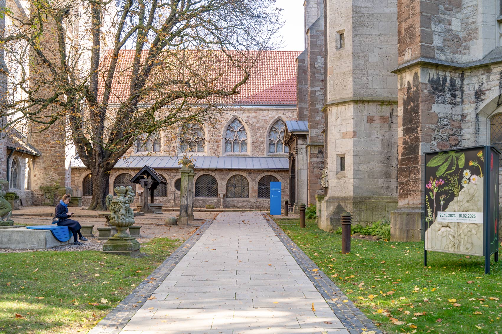 Im Hintergrund: Person sitzt auf blauer Fläche, dahinter blaue Stehle des Orientierungssystems