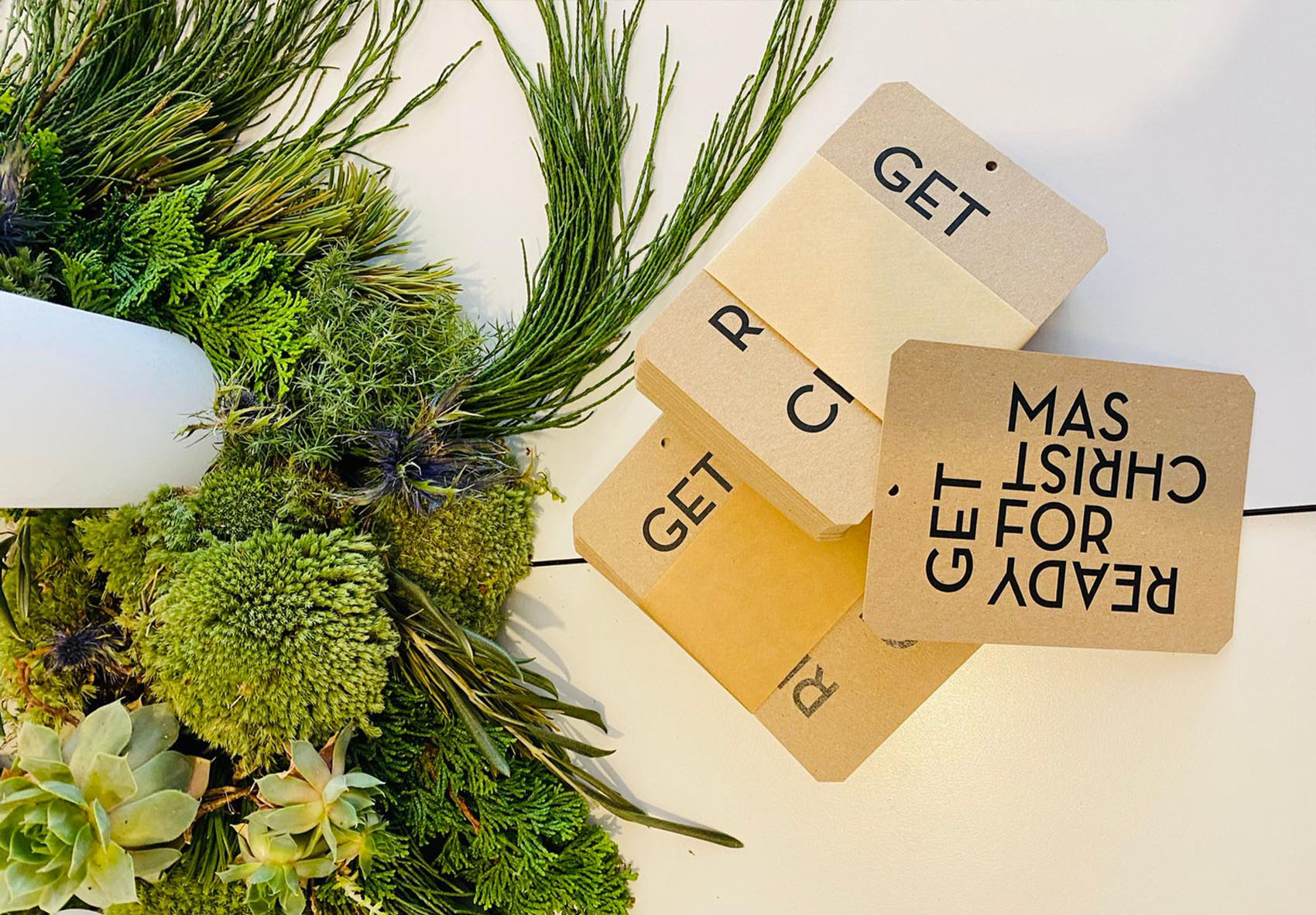 Anhänger „GET READY FOR CHRISTMAS“ arrangiert neben einem Adventskranz