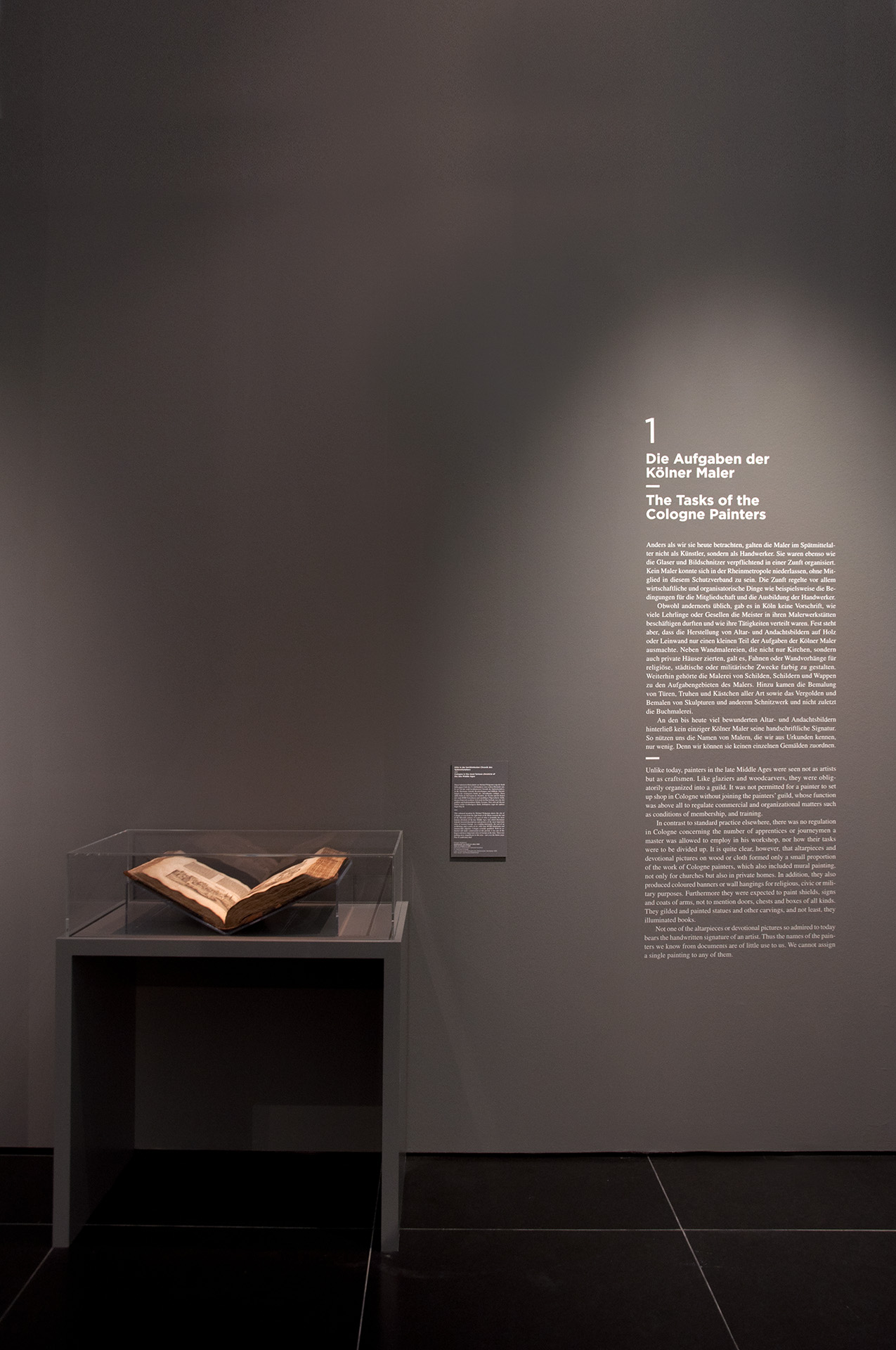 Blick auf schwarze Wand mit weißem Text "Die Aufgaben der Kölner Maler"
