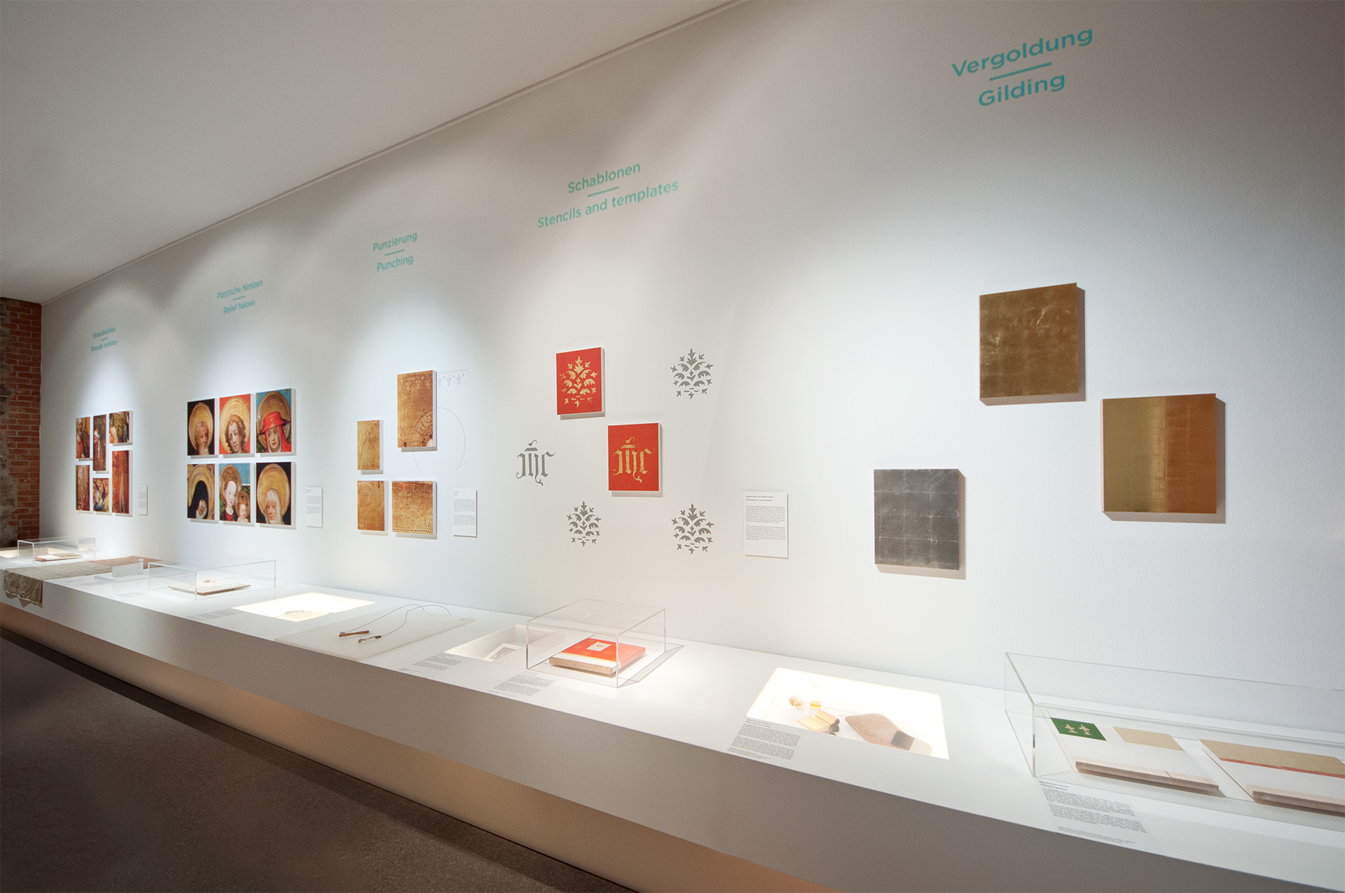 Blick auf weiße Ausstellungswand mit langem Pultmöbel davor auf dem sich verschiedene Vitrinen und Exponate befinden