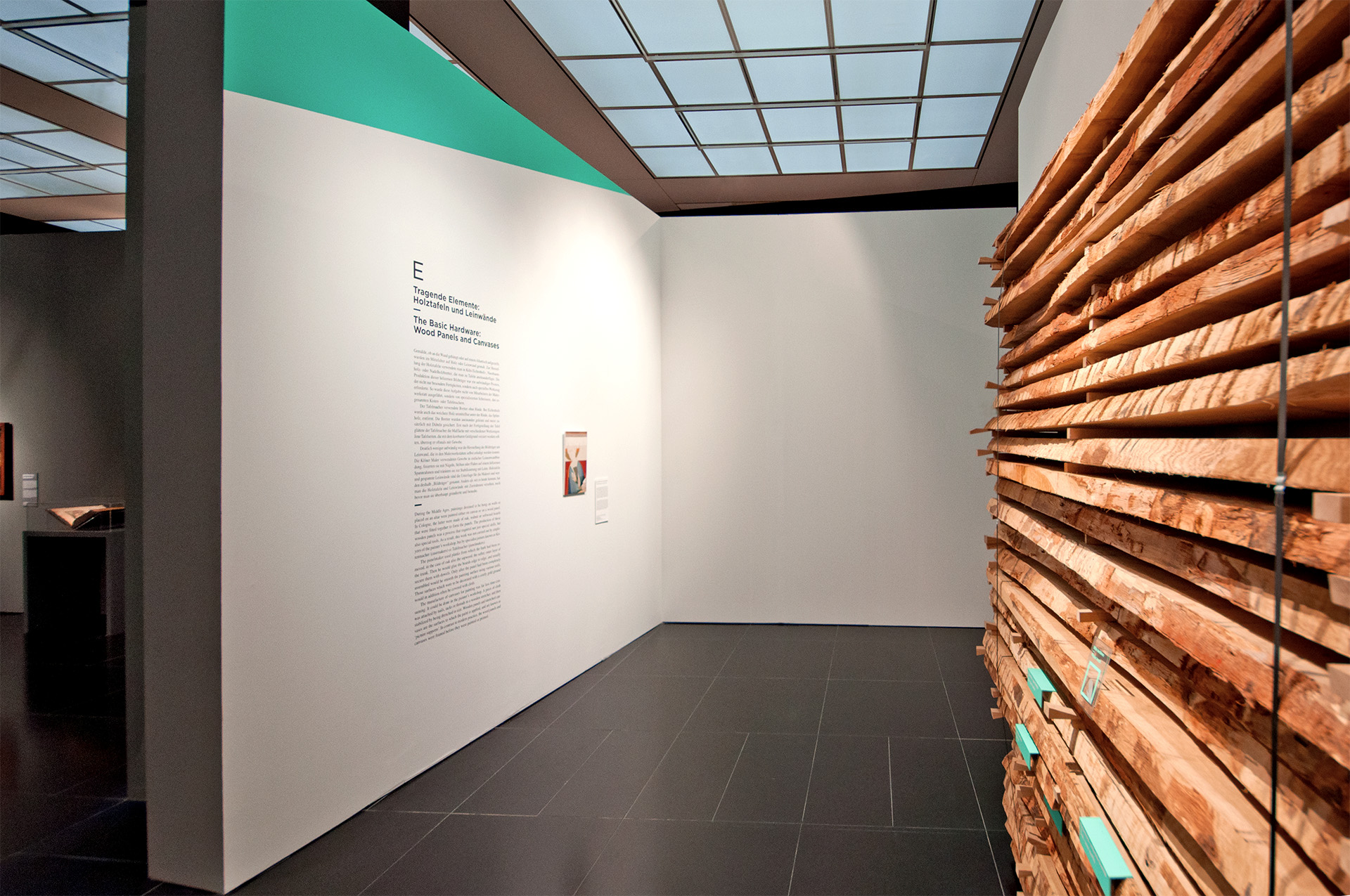 Blick auf weiße Wand mit schwarzem Text "Tragende Elemente: Holztafeln und Leinwände"