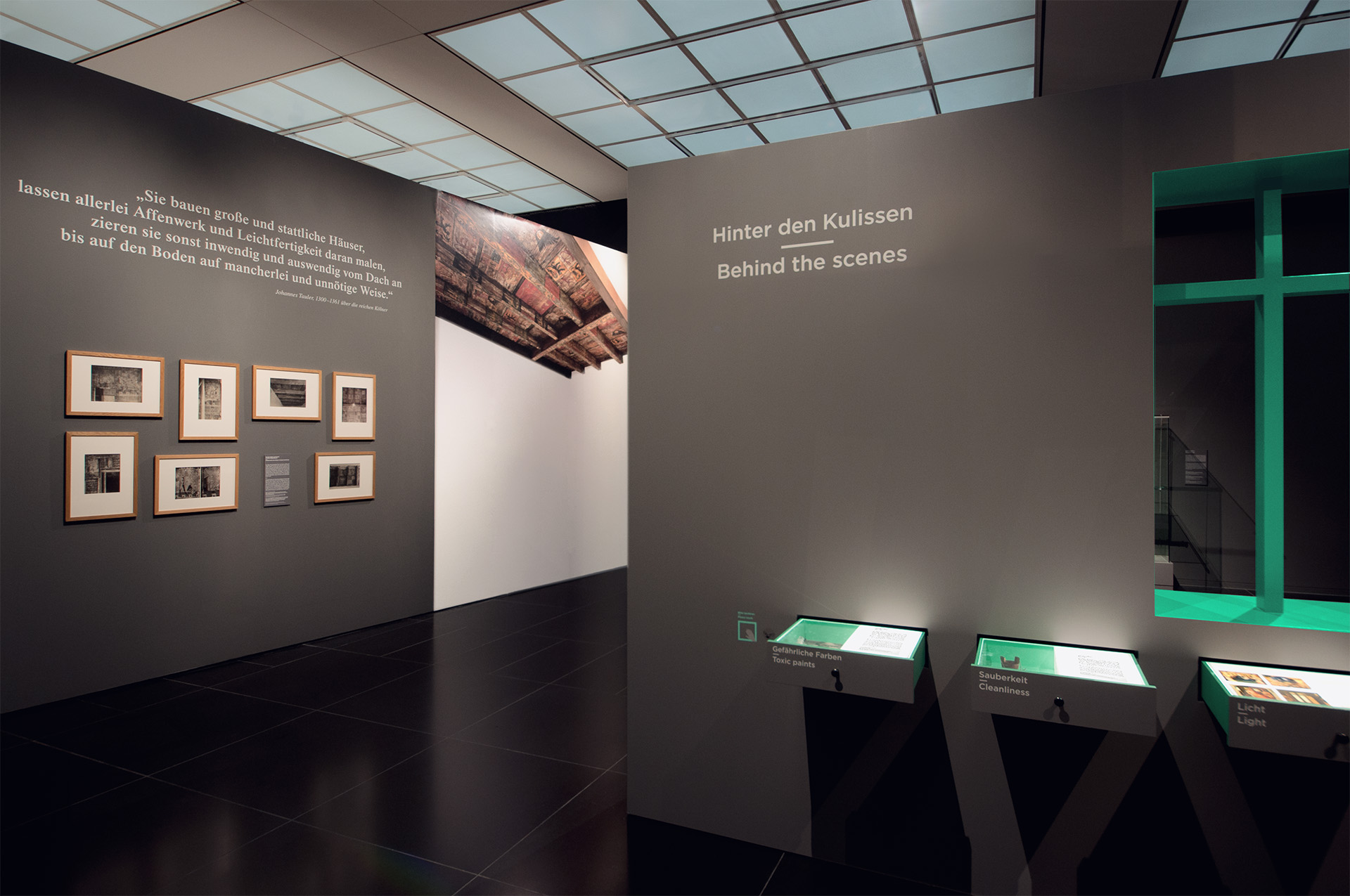 Blick in Ausstellung auf dunkelgraue Ausstellungswände mit Auszügen, Bilder und Pultvitrinen