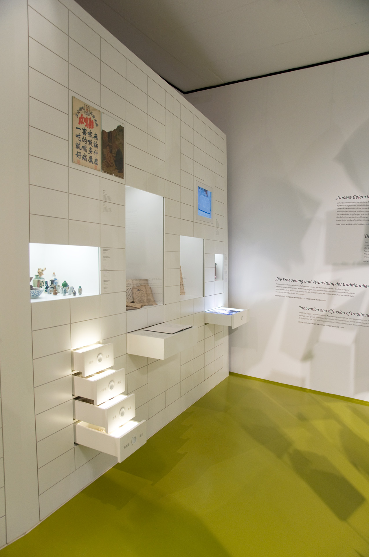 Ausstellungswand mit herausgezogenen Schubkästen. Darüber Einlassvitrinen.