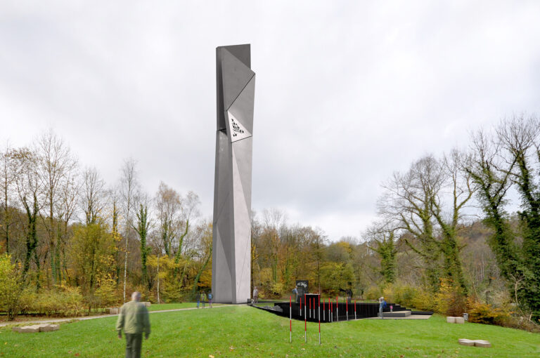 Blick auf einen Park indem eine monolithische Architektur steht. Diese Architektur ist doppelt so hoch, wie die Bäume um sie herum.