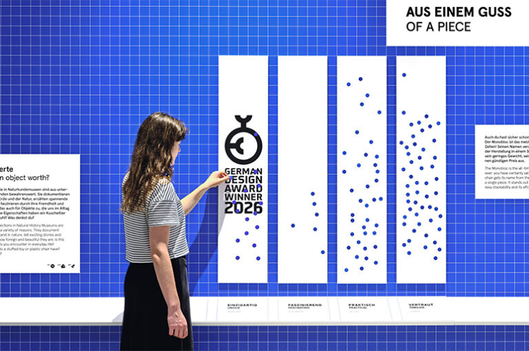 Frau, die an einer partizipativen Wand Sticker aufklebt. Über das Foto ist das Logo als German Design Award Winner 2026 gelegt.
