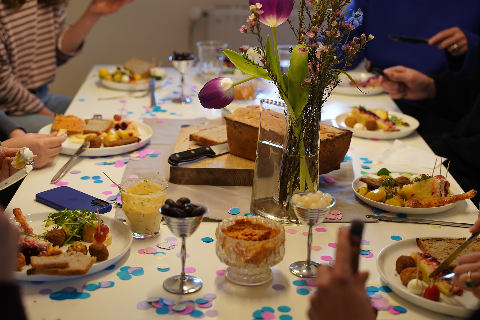Blick auf einen vollen Tisch mit vielen Menschen, vollen Tellern und buntem Konfetti.