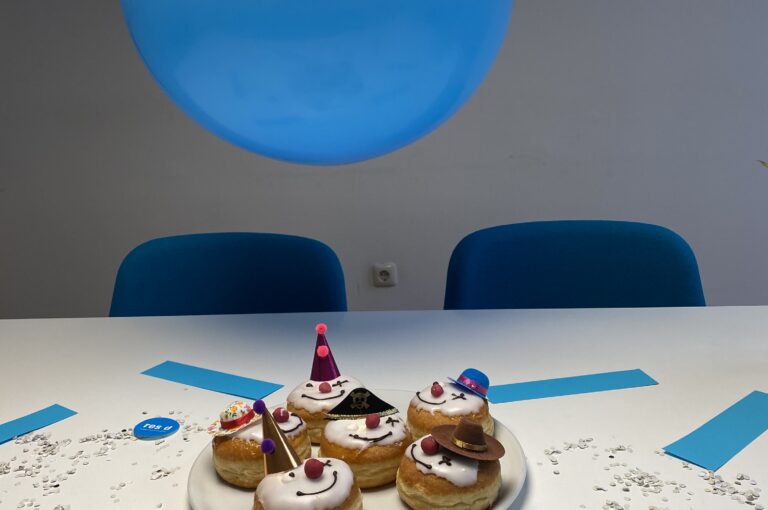 Muffins mit Clownsgesichtern darüber ein blauer Luftballon und rundherum Konfetti