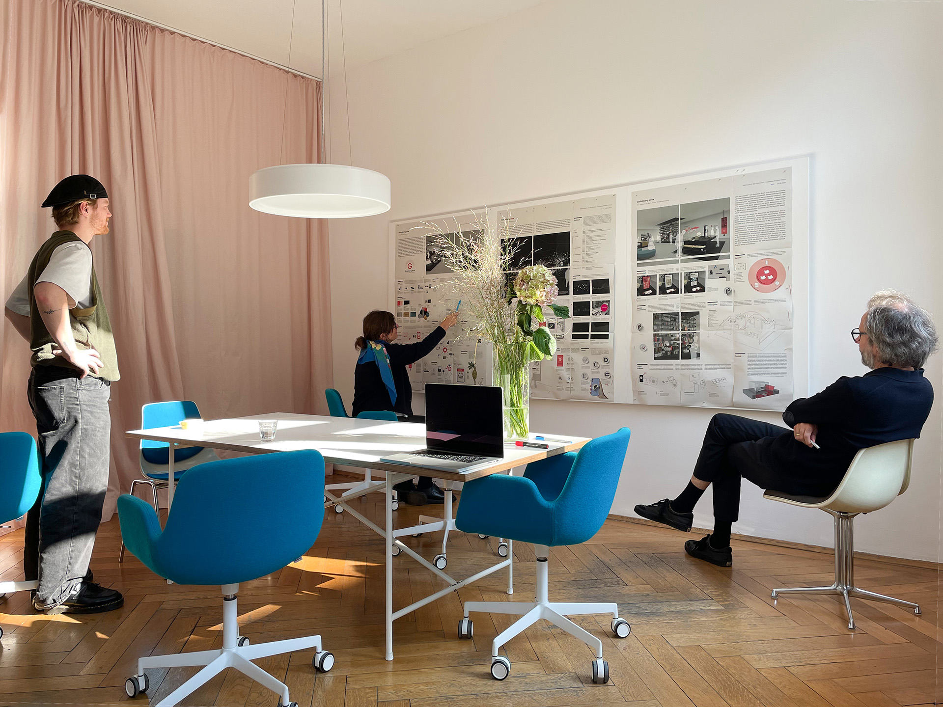 Blick in den alten Besprechungsraum von res d, indem Rebecca Schröder, Ingo Plato und Damian Pläne eines Wettbewerbs betrachten und sich austauschen.