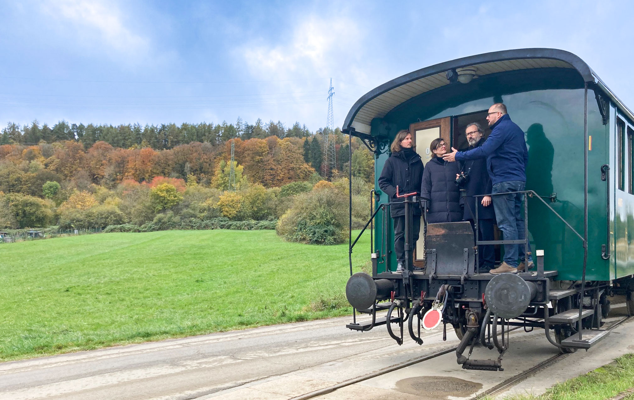 Alexander Hesse, Rebecca Schröder und Ingo Plato stehen am Hinterausgang eines alten grünen Waggons und lassen sich von einem Vereinsmitarbeiter etwas erklären