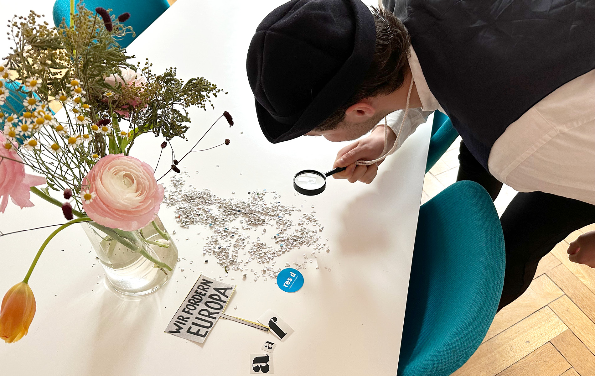 res d Mitarbeiter verkleidet als Detektiv untersucht mit seiner Lupe Konfetti auf dem Tisch