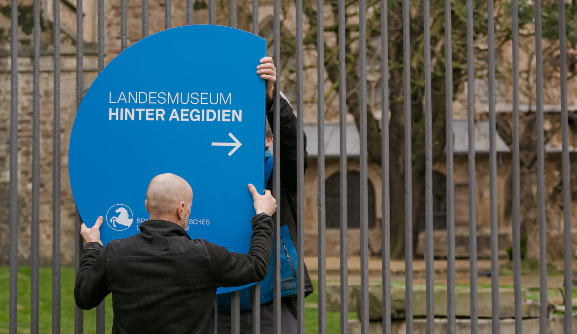 Handwerker bei der Montage eines runden Orientierungsschildes in Blau