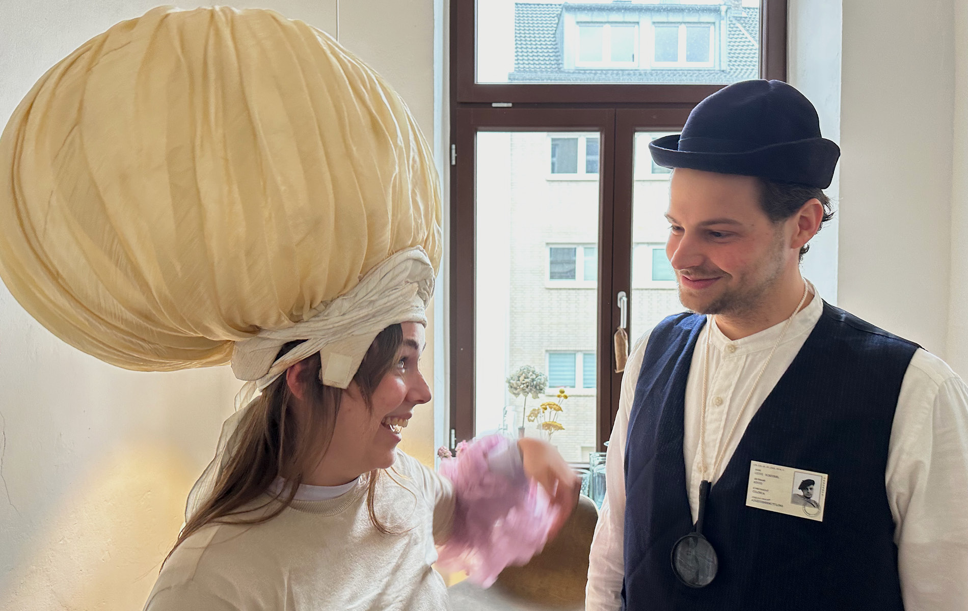 links: res d Mitarbeiterin mit einer überdimensionalen Zwiebel auf dem Kopf, rechts: res d Mitarbeiter verkleidet als Detektiv