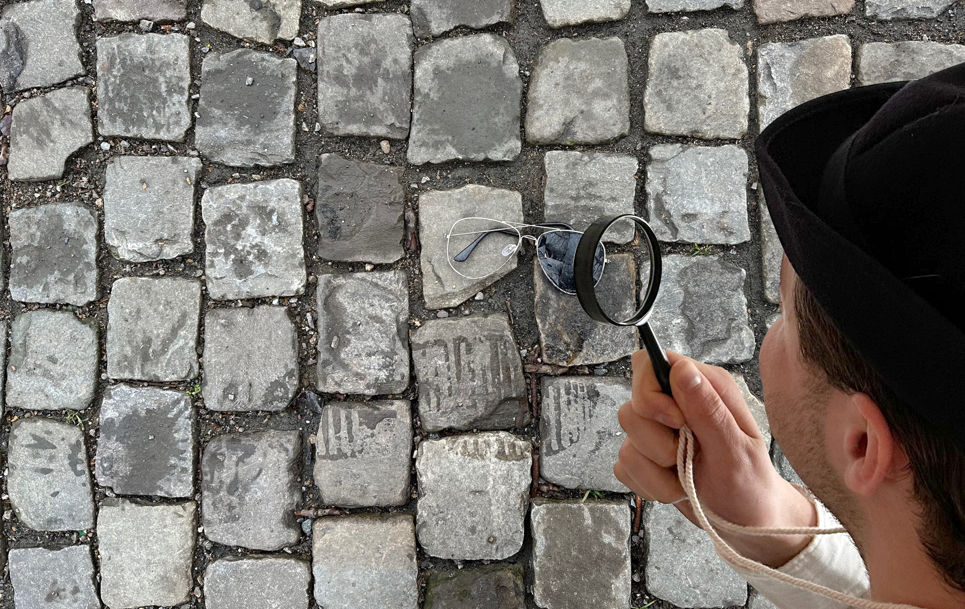 res d Mitarbeiter verkleidet als Detektiv untersucht mit seiner Lupe eine kaputte Sonnenbrille auf der Straße