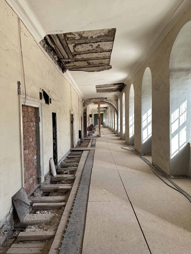 Sanierungsarbeiten in einem langen historischen Flur mit geöffneter Decke, freigelegtem Boden und Rundbogenfenstern